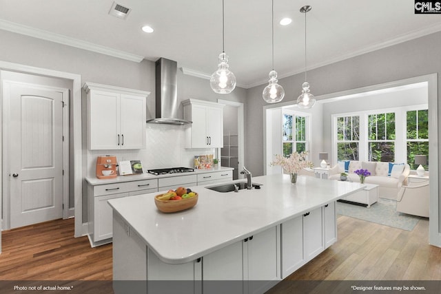 kitchen featuring wall chimney range hood, hardwood / wood-style floors, an island with sink, white cabinetry, and sink