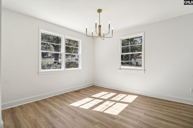 empty room with hardwood / wood-style flooring and a notable chandelier