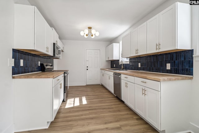 kitchen featuring white cabinetry, stainless steel appliances, sink, and wood counters