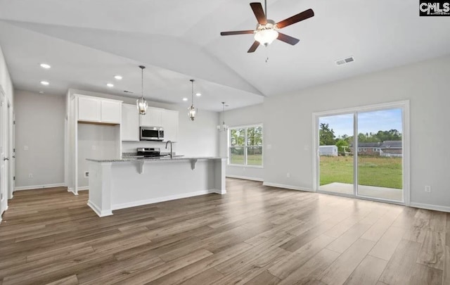 kitchen with hanging light fixtures, stainless steel appliances, hardwood / wood-style floors, light stone countertops, and white cabinets