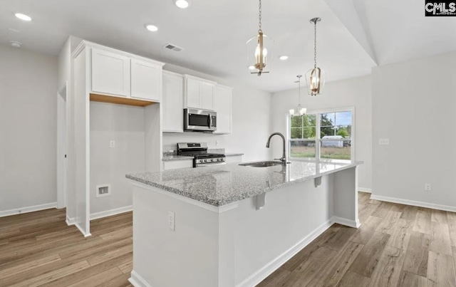 kitchen featuring white cabinets, a center island with sink, appliances with stainless steel finishes, light hardwood / wood-style flooring, and pendant lighting