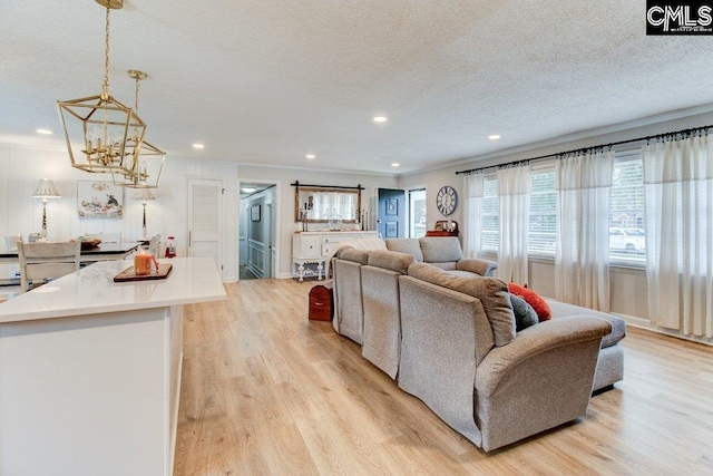 living room with a chandelier, crown molding, a textured ceiling, and light wood-type flooring