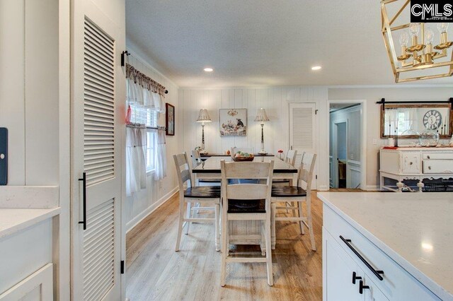 kitchen with light hardwood / wood-style flooring, a barn door, decorative light fixtures, white cabinetry, and light stone counters