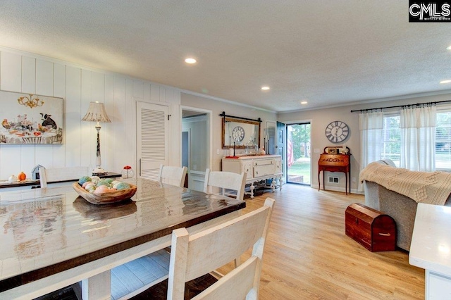 dining space featuring light hardwood / wood-style floors, ornamental molding, and a barn door