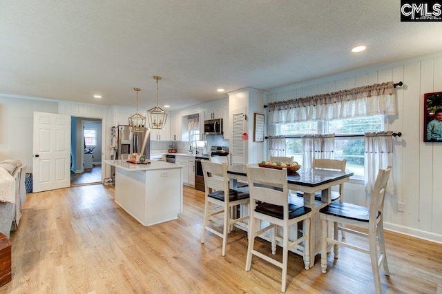 kitchen featuring a kitchen island, hanging light fixtures, stainless steel appliances, white cabinets, and light hardwood / wood-style floors