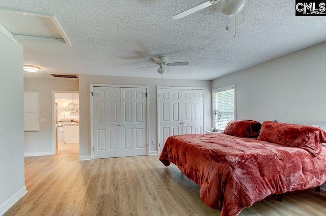 bedroom featuring light hardwood / wood-style floors, a textured ceiling, multiple closets, and ceiling fan