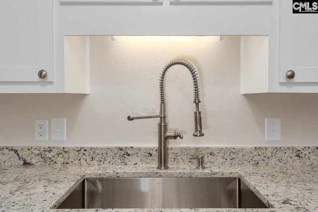 room details featuring light stone counters, sink, and white cabinets