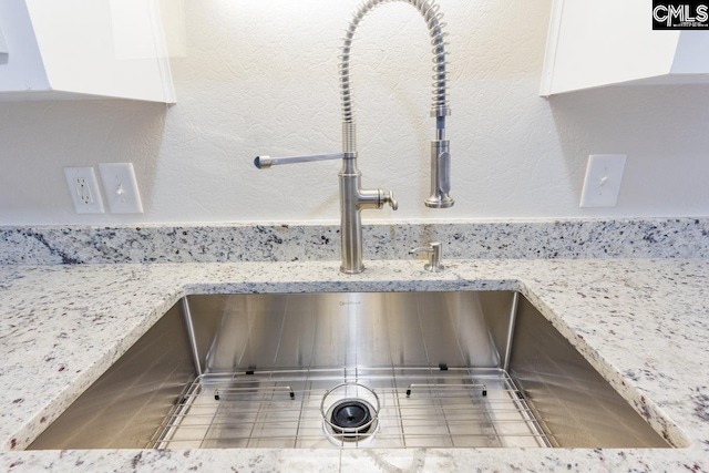 interior details with tile patterned floors, light stone countertops, sink, and white cabinets