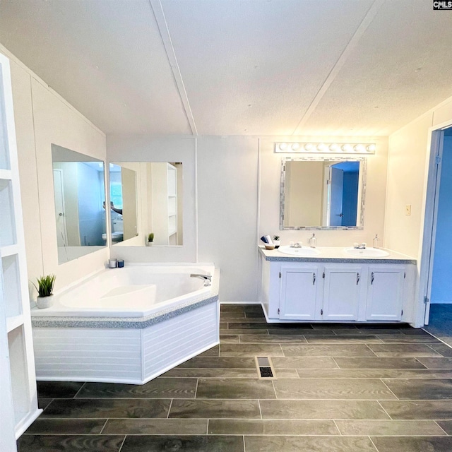 bathroom with tiled bath, vanity, and a textured ceiling