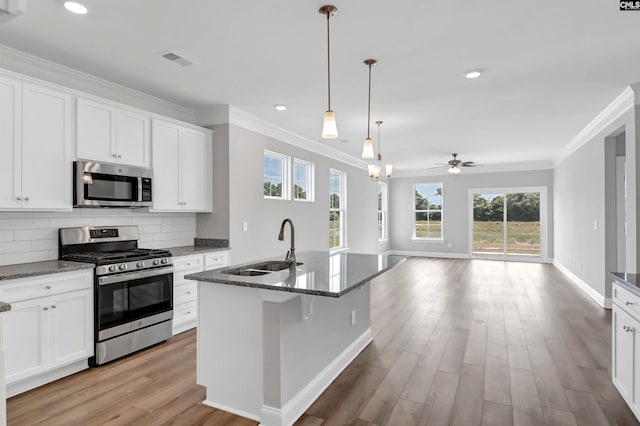 kitchen featuring light hardwood / wood-style floors, white cabinetry, appliances with stainless steel finishes, dark stone counters, and a kitchen island with sink