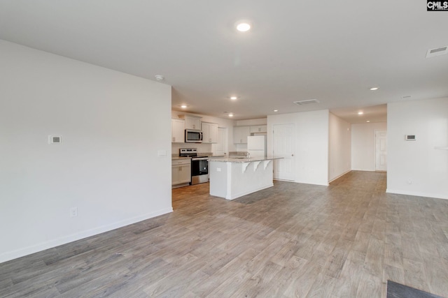 kitchen with stainless steel appliances, light hardwood / wood-style floors, white cabinetry, a breakfast bar area, and a kitchen island