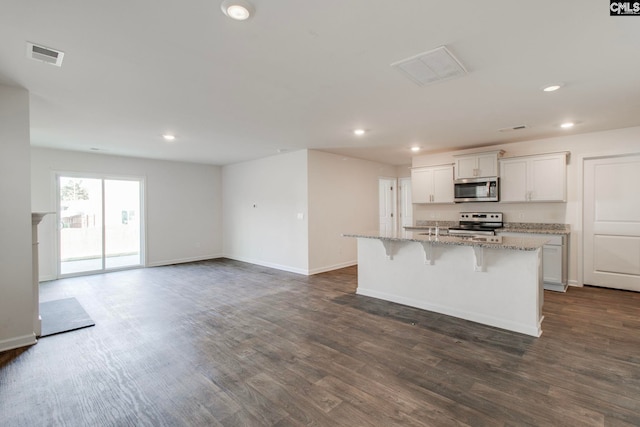 kitchen featuring stainless steel appliances, a kitchen breakfast bar, dark hardwood / wood-style floors, an island with sink, and white cabinets