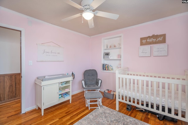 bedroom featuring ornamental molding, a nursery area, ceiling fan, and light hardwood / wood-style flooring