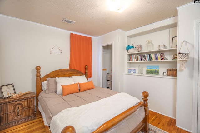 bedroom with a textured ceiling, light hardwood / wood-style flooring, and ornamental molding