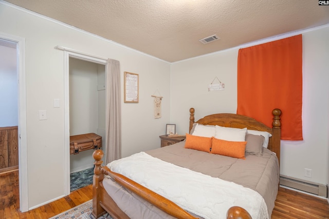 bedroom featuring wood-type flooring, a textured ceiling, a baseboard heating unit, and crown molding