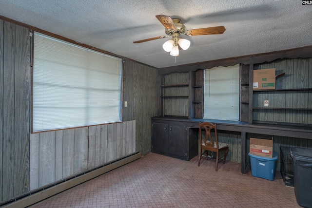 unfurnished office with ceiling fan, baseboard heating, carpet flooring, a textured ceiling, and wooden walls