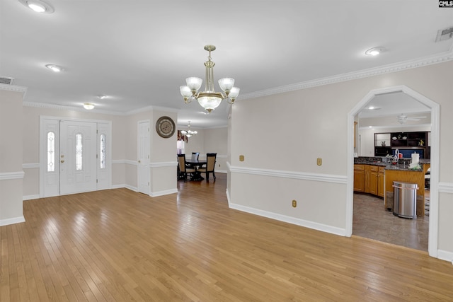 unfurnished living room featuring ceiling fan with notable chandelier, light wood-type flooring, and crown molding