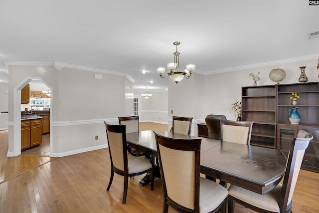 dining space featuring light wood-type flooring, a chandelier, sink, and crown molding