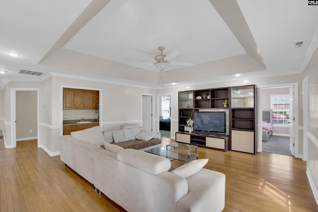 living room with light hardwood / wood-style floors, ceiling fan, crown molding, and a tray ceiling