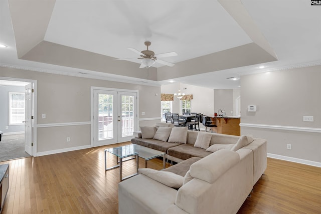 living room with light wood-type flooring, french doors, a raised ceiling, and ceiling fan with notable chandelier