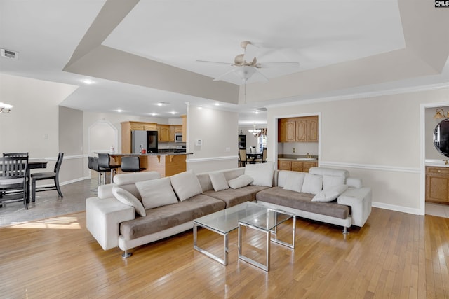 living room with ceiling fan with notable chandelier, light hardwood / wood-style flooring, and a tray ceiling