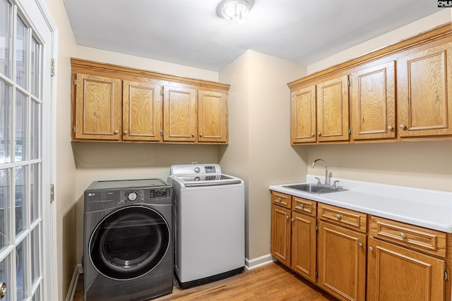 clothes washing area with washing machine and dryer, cabinets, sink, and light hardwood / wood-style floors