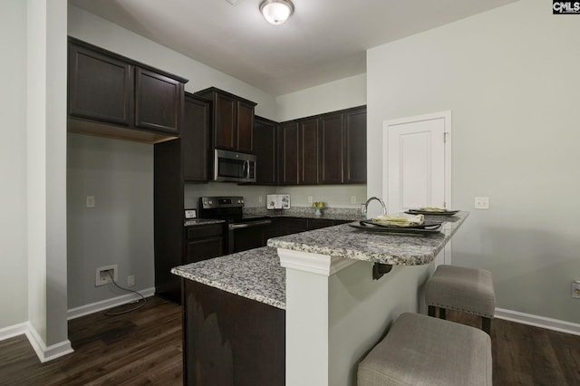 kitchen featuring dark wood-type flooring, kitchen peninsula, a breakfast bar, light stone countertops, and appliances with stainless steel finishes