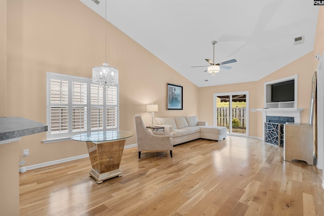 living room with light wood-type flooring, ceiling fan with notable chandelier, and high vaulted ceiling