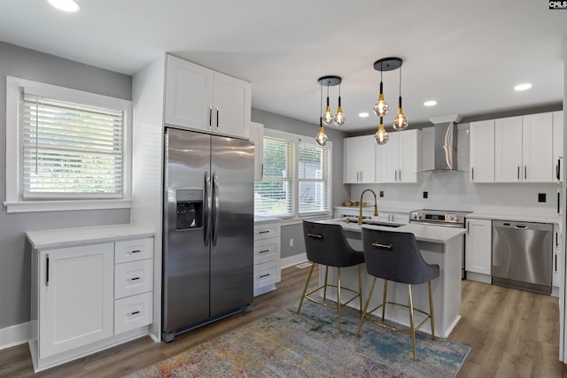 kitchen featuring white cabinets, wall chimney exhaust hood, a kitchen island with sink, and appliances with stainless steel finishes