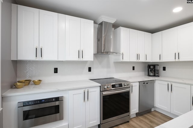 kitchen with light hardwood / wood-style floors, appliances with stainless steel finishes, white cabinets, wall chimney range hood, and decorative backsplash