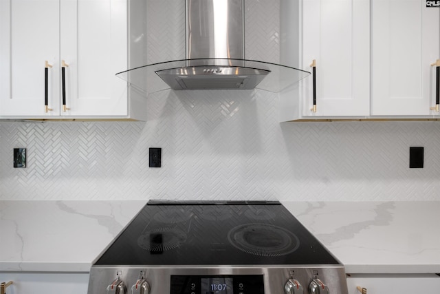 kitchen with white cabinetry, wall chimney range hood, light stone countertops, and black range oven