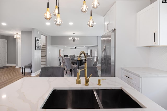 kitchen with pendant lighting, white cabinetry, stainless steel refrigerator with ice dispenser, and light stone counters