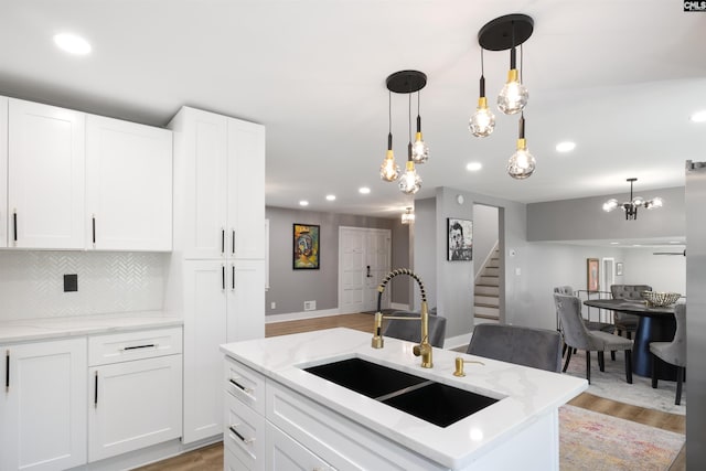 kitchen with light hardwood / wood-style floors, sink, a kitchen island with sink, white cabinetry, and decorative light fixtures