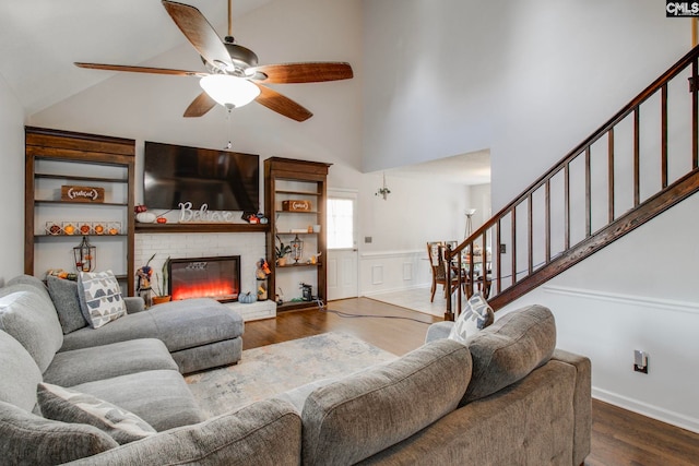 living room featuring dark wood-type flooring, high vaulted ceiling, ceiling fan, and a brick fireplace