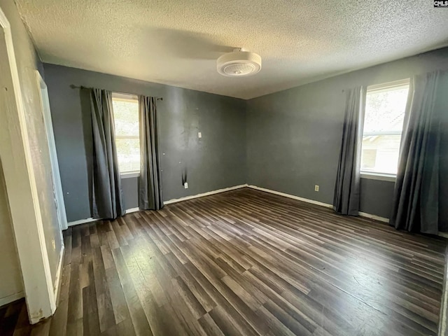 empty room featuring dark wood-type flooring, a textured ceiling, and a healthy amount of sunlight