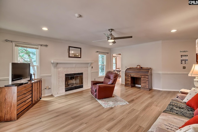 living room featuring a wealth of natural light, a tiled fireplace, light hardwood / wood-style floors, and ornamental molding