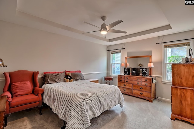 bedroom with light colored carpet, ceiling fan, and a tray ceiling