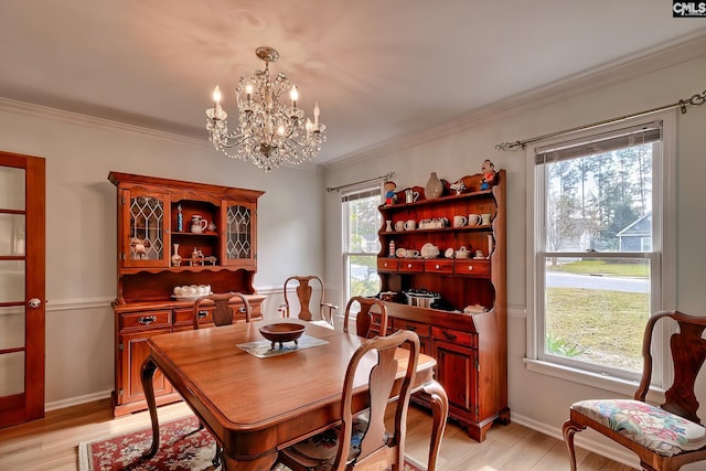 dining room featuring light wood-type flooring, a wealth of natural light, an inviting chandelier, and ornamental molding