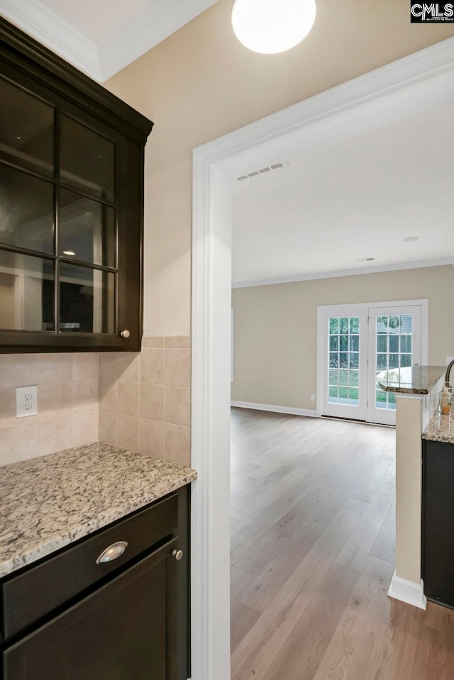 bar with dark brown cabinets, light hardwood / wood-style flooring, light stone counters, and tasteful backsplash