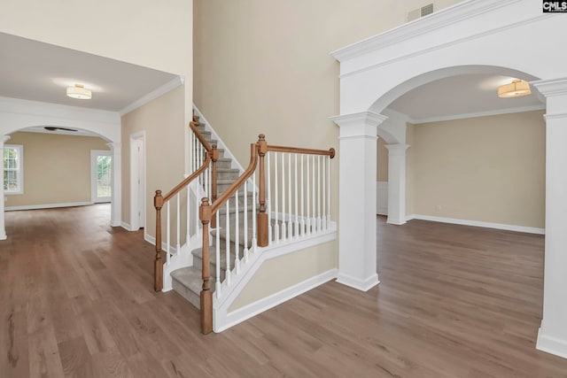 staircase featuring hardwood / wood-style floors, crown molding, and decorative columns