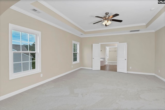 unfurnished bedroom with a walk in closet, crown molding, a tray ceiling, light colored carpet, and ceiling fan