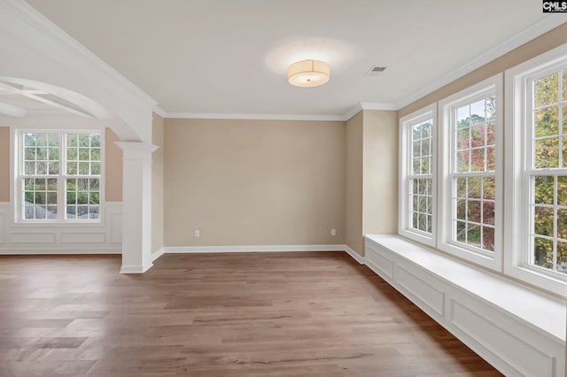 unfurnished room featuring decorative columns, hardwood / wood-style floors, and crown molding