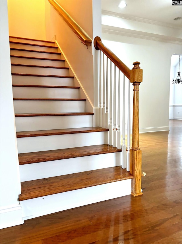 stairway featuring wood-type flooring, an inviting chandelier, and ornamental molding