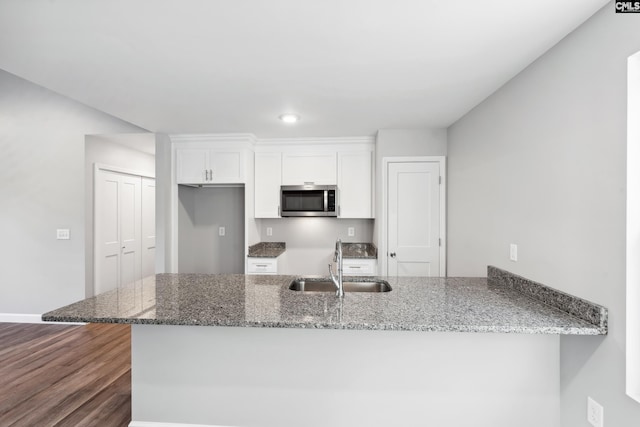 kitchen with dark wood-type flooring, white cabinets, sink, stone countertops, and kitchen peninsula