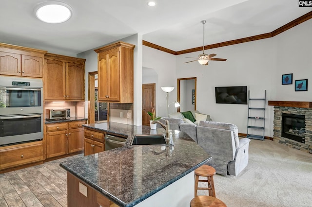 kitchen with a fireplace, appliances with stainless steel finishes, sink, light hardwood / wood-style floors, and ceiling fan