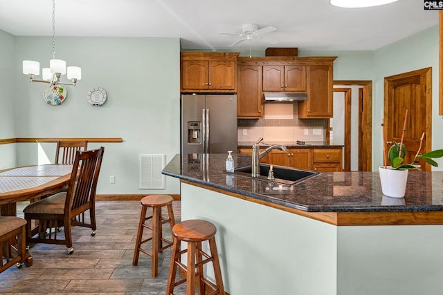 kitchen featuring sink, ceiling fan with notable chandelier, decorative light fixtures, dark wood-type flooring, and stainless steel fridge with ice dispenser