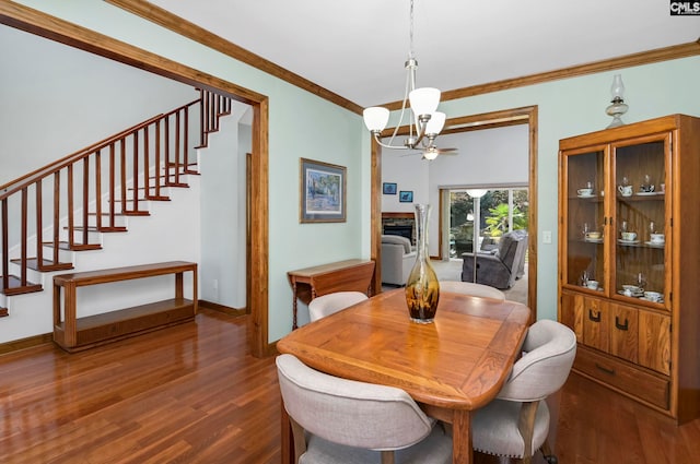 dining area featuring dark wood-type flooring, a chandelier, ornamental molding, and a fireplace