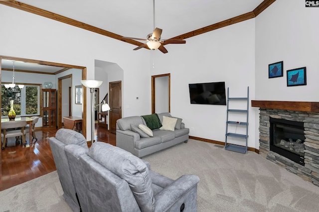 living room featuring ceiling fan, wood-type flooring, a stone fireplace, and crown molding