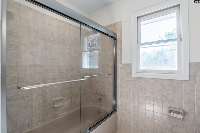 bathroom featuring tile walls and combined bath / shower with glass door