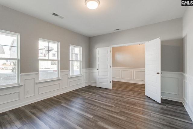 empty room featuring a wainscoted wall, visible vents, and dark wood-type flooring